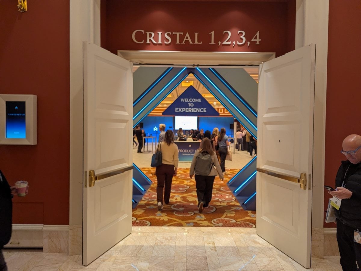 Open double doors at the Wynn Las Vegas reveal the entrance to Medallia Experience ’26, with a blue geometric archway reading “Welcome to Experience” and attendees walking into the conference space.