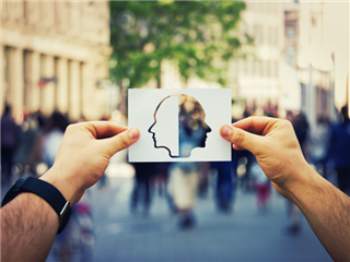 A man in a common area looking at people through a sheet of paper with a human face cut out of it - customer behavior concept