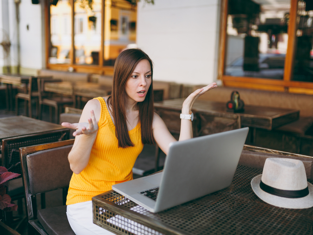 Frustrated woman in outdoors street coffee shop cafe sitting at table working on laptop computer