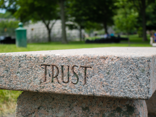 A concrete bench with the word trust etched in the side in a cematary