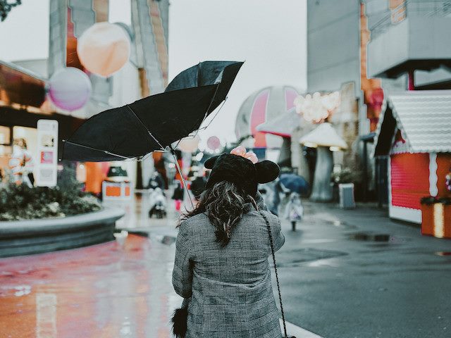 woman walking through windy city with broken umbrella overhead