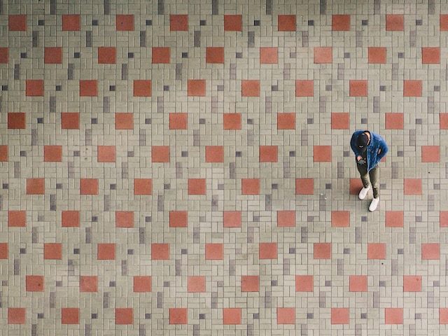 man standing on patterned tile floor, looking intently at his phone
