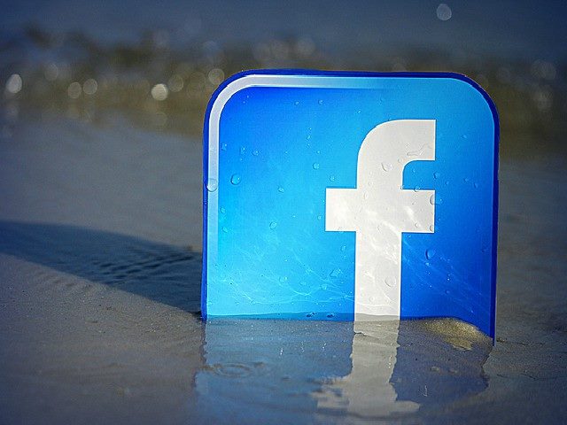 Facebook logo stuck in the sand on a beach.