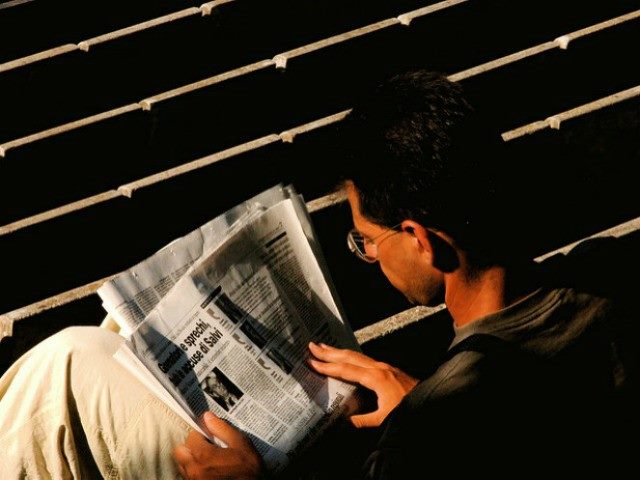 Man sitting down reading a newspaper.