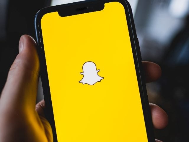 A holds a smartphone displaying teh yellow and white Snapchat logo in piece about AI embedded in Snapchat+ subscription. 