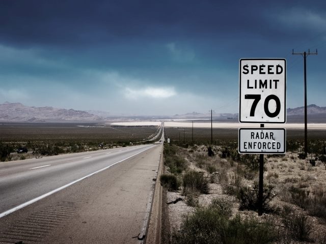 A speed limit sign for 70 MPH is poste along an empty road.