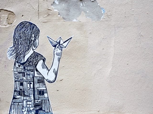 wheatpaste art on wall of girl  holding paper airplane