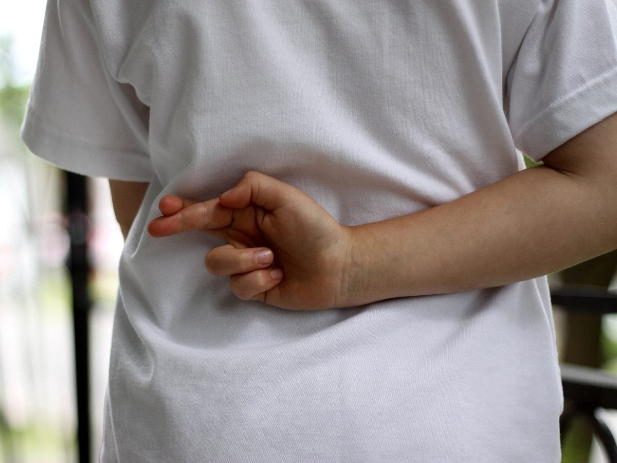 Person standing with their back partially turned, holding fingers crossed behind their back, suggesting dishonesty or a hidden promise.