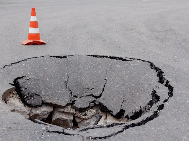 sinkhole  in a street with orange hazard cone nearby