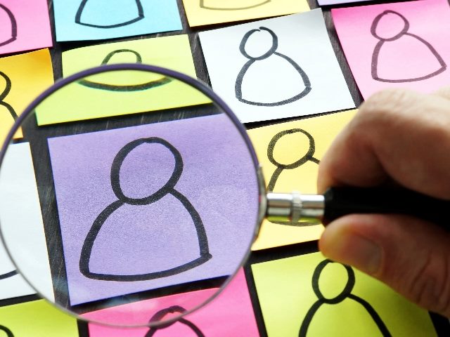 A hand holds a magnifying glass over simple drawn figures of people on colorful sticky notes in piece about using customer insights for product development. 