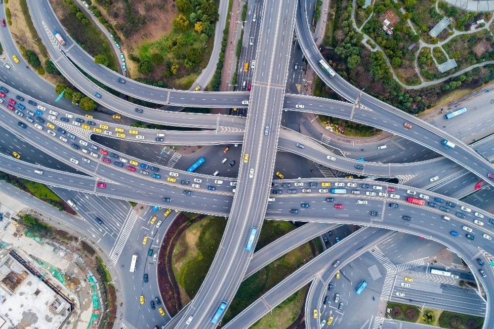 Aerial view of a complex, multi-level highway interchange showing numerous cars on intersecting roads, symbolizing the intersection of the customer journey, the employee journey and the life journey in a bustling, interconnected network.