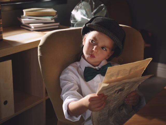 young girl sitting down holding a newspaper.