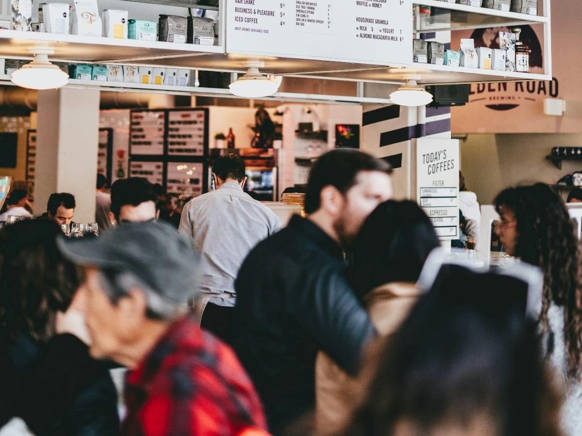 Customers in line and sitting down talking at coffee shop.