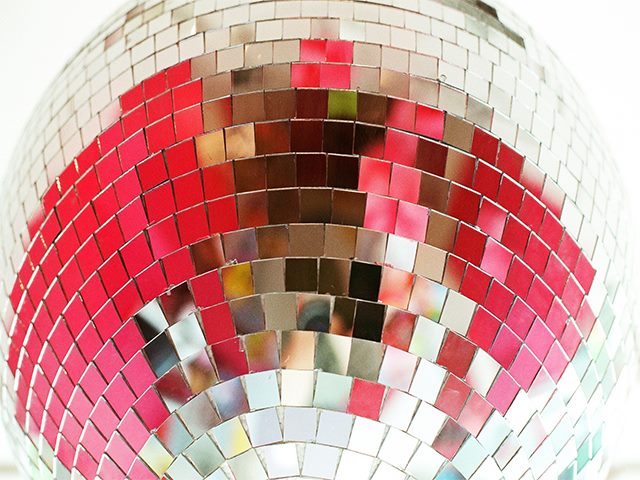 Up-close image of a mirrored disco ball, reflecting pink and grey colors. 
