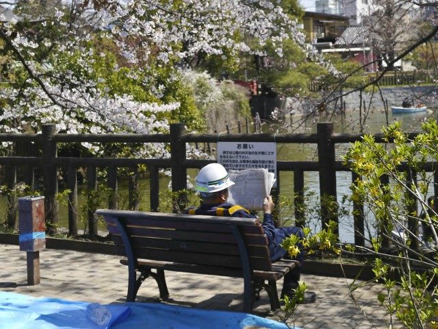 Man wearing a hard hat sitting on a bench reading a newspaper