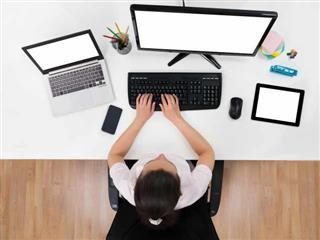 A person at their desk with multiple computers and mobile devices