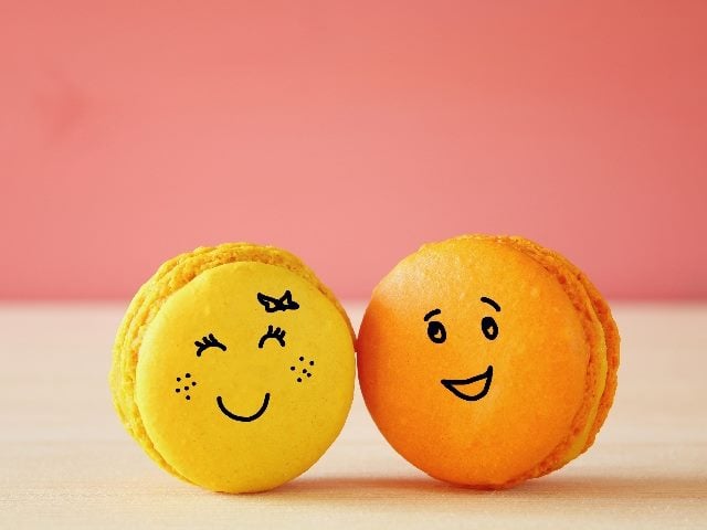 Image of two macaroons, one yellow and one orange, with drawn smiley faces.