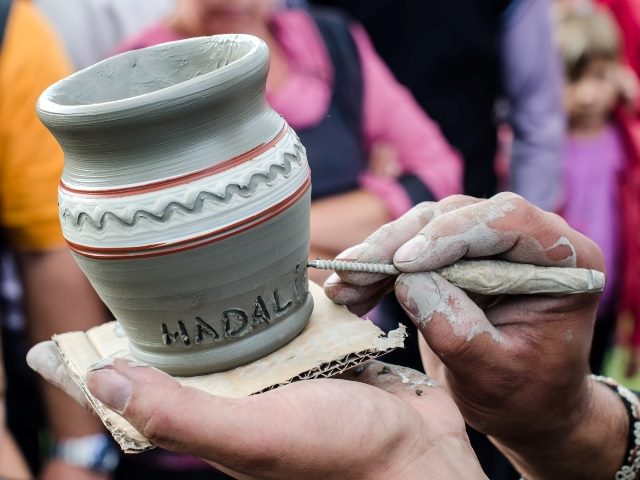 Closeup on artist hands personalizing a clay jug with name. 