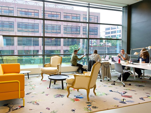 A brightly-colored decorated conference room with four coworkers discussing on the right. 