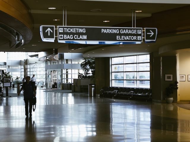 person walking through hallways of airport with direction signs overhead