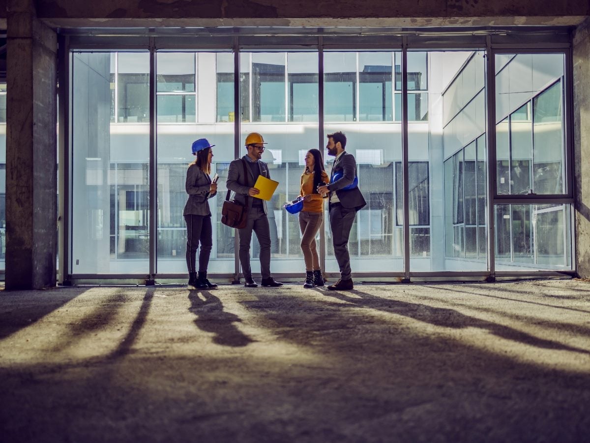 Team of four architects reviewing plans inside a modern commercial building under construction.