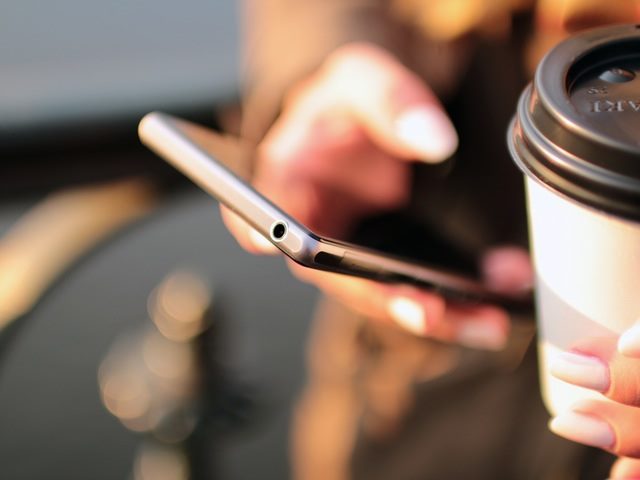person holding a coffee cup and using a phone