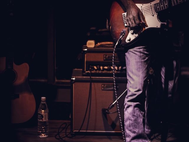 man standing with a guitar and two amps