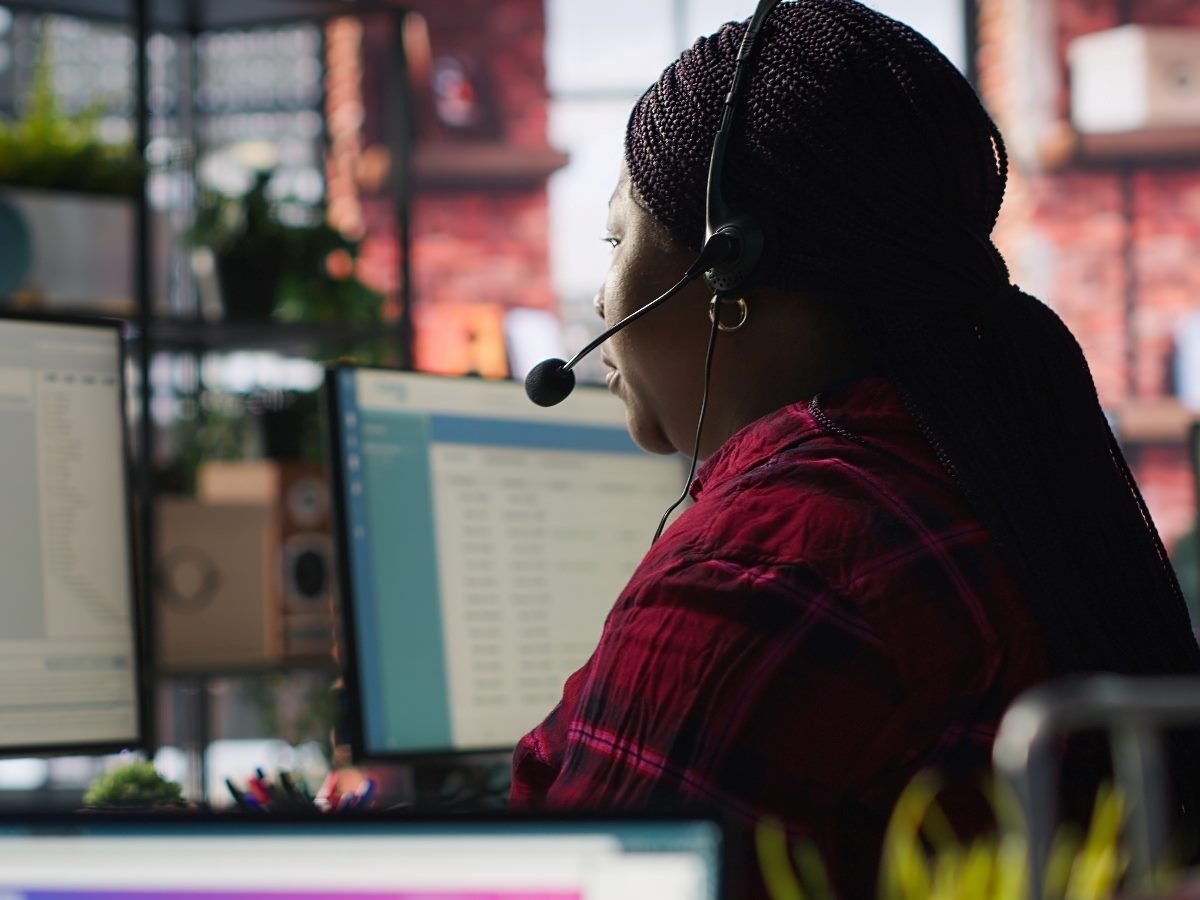 IT support specialist at PC in office helping customers during call, troubleshooting errors.