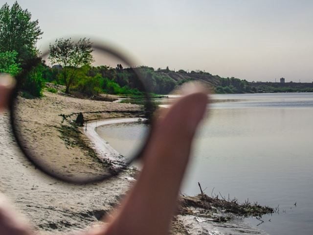 A hand holding a lens over a beach scene, bringing it into tight focus - Clarity concept