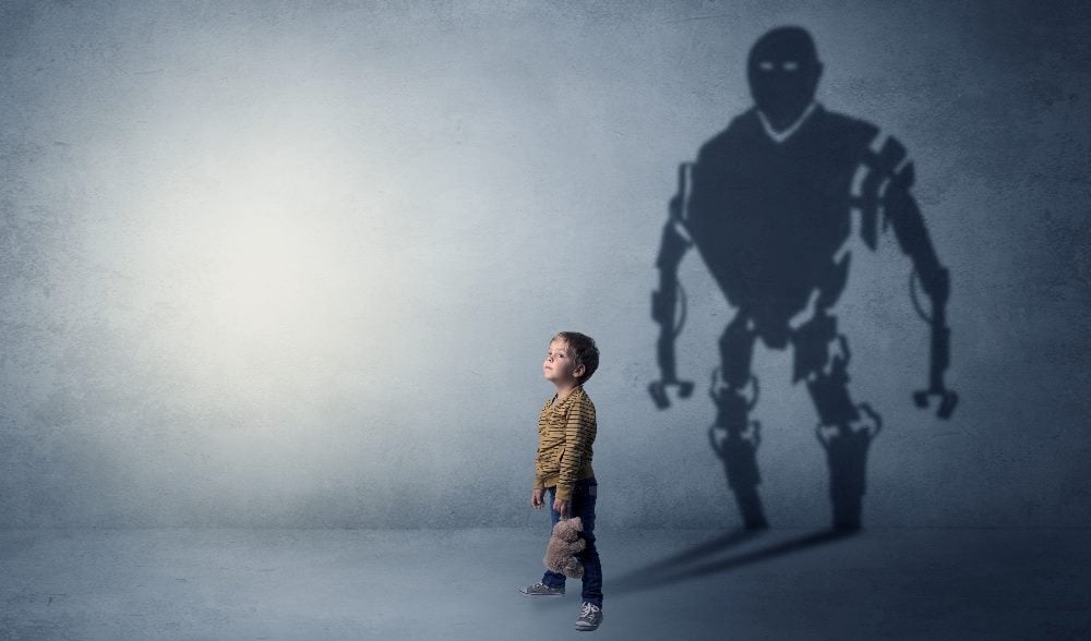 A young boy stands in front of a wall on which a huge, frightening robot shadow is visible, suggesting the dangers of AI technology.