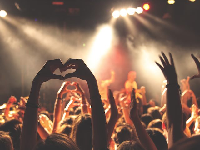 fan in concert crowd holding hands up in heart shape