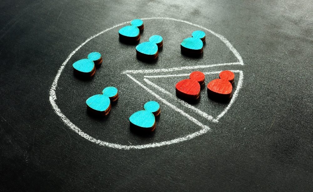 Small red and blue wooden cutouts of customer icons have been placed on a pie chart drawn in white chalk on a blackboard in piece about customer data segmentation.