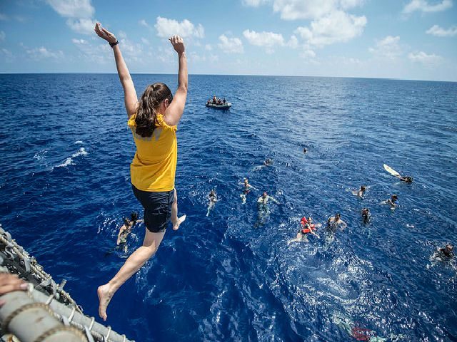 woman jumping off a cliff into a body of water with people already in the water