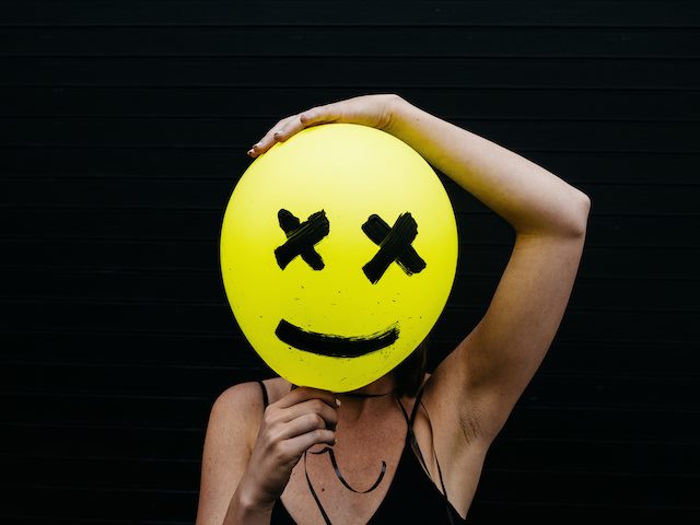person holding a balloon in front of their face with a face drawn on it
