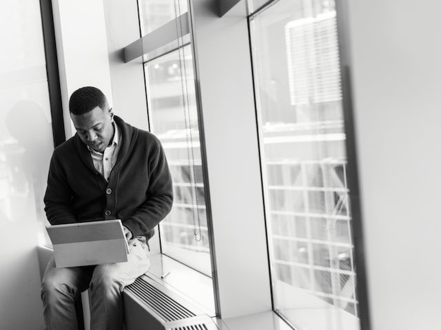 person working on their laptop while sitting in a window