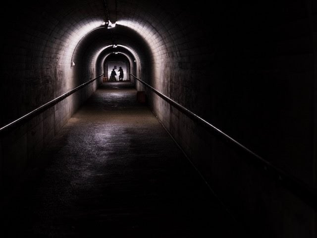 two people standing in  light at the end of a long tunnel