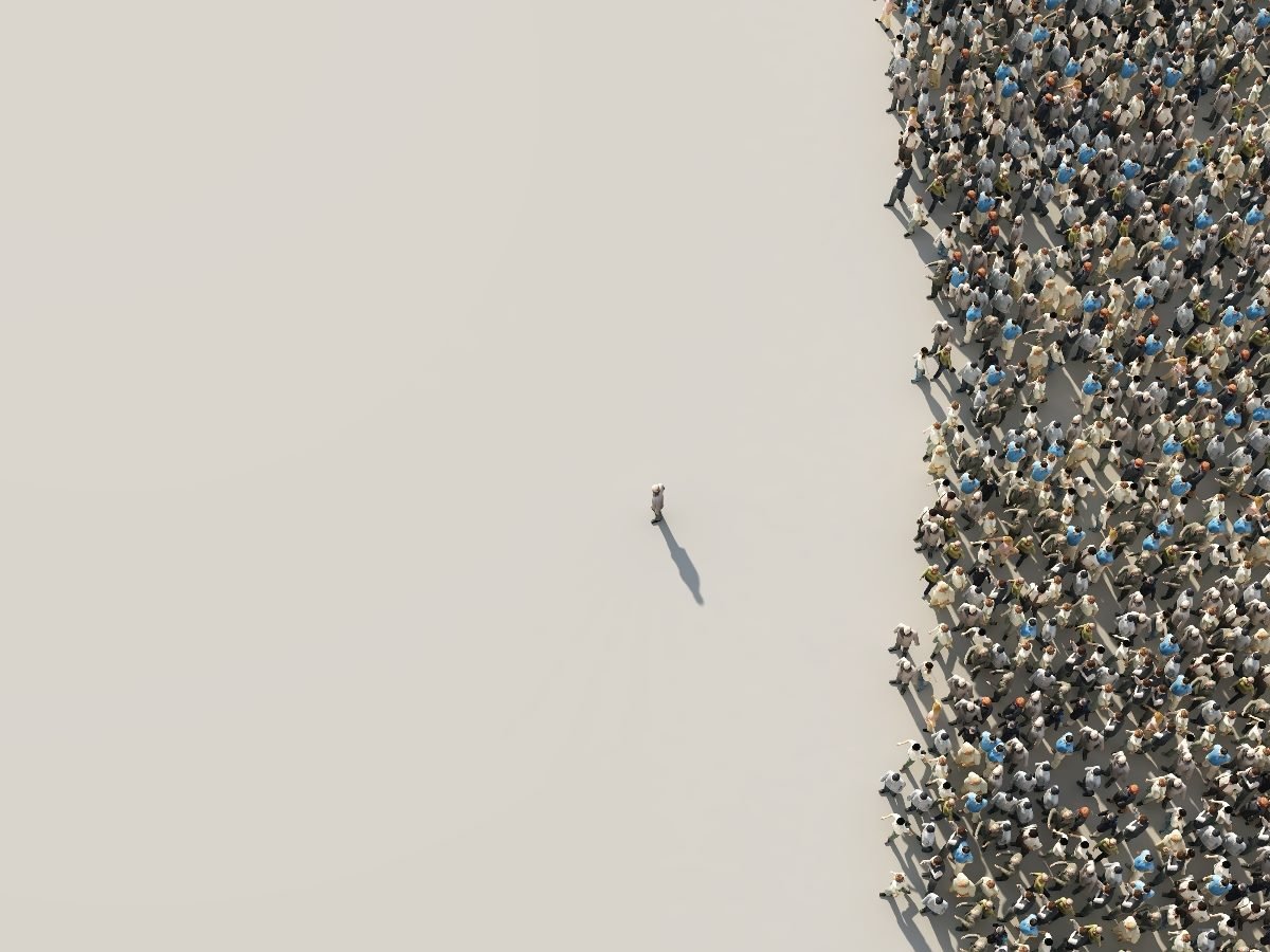 A single person stands apart on an open expanse facing a large crowd of people clustered together, symbolizing leadership, influence and standing out from the group.