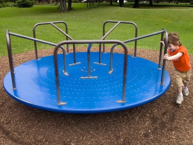 Young boy pushes a merry-go-round. 