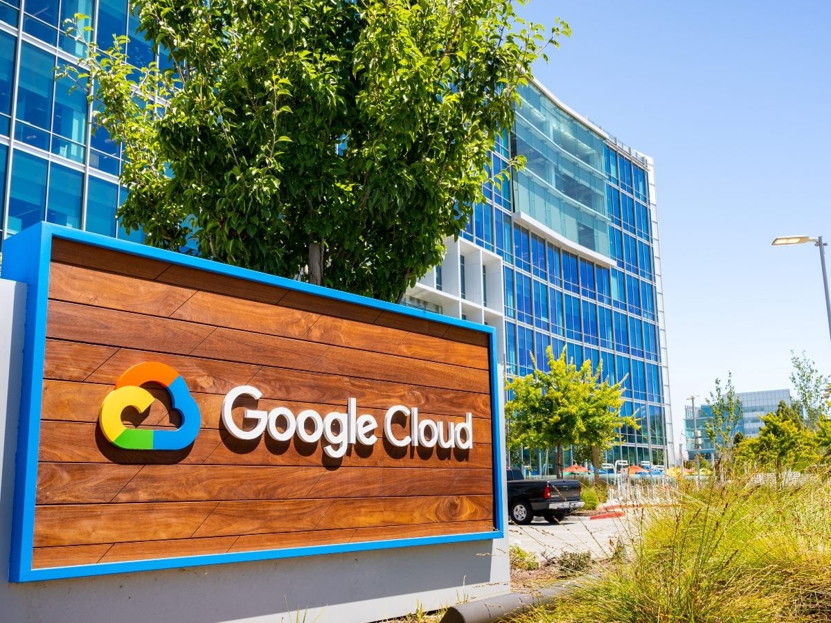 Google Cloud signage with its cloud logo displayed on a wooden sign in front of the company's glass office building.