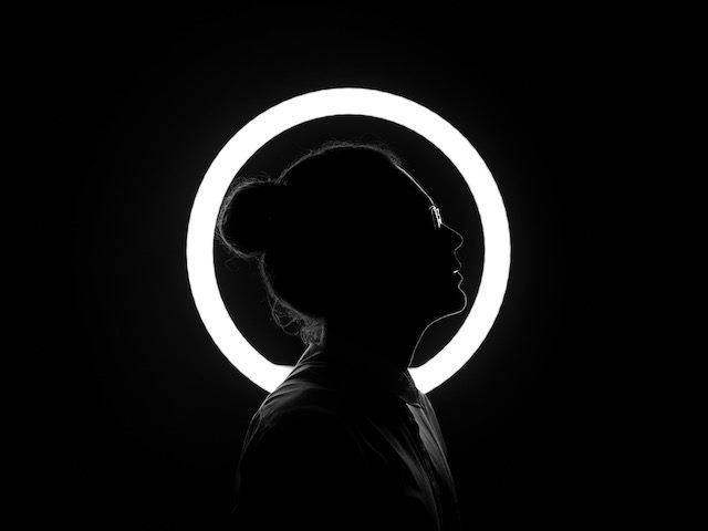 person in silhouette standing in front  of  a  circular neon light
