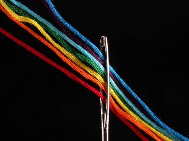 Multi-colored thread being passed through a needle. 