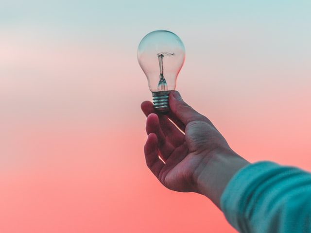 person holding lightbulb against a blue and pink sky