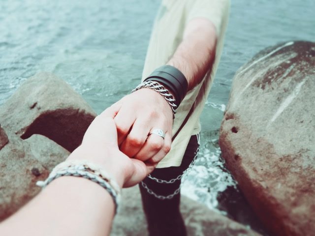 one person supporting another on a rocky bank