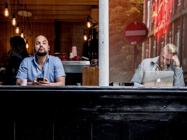 two men sitting in a cafe window on devices