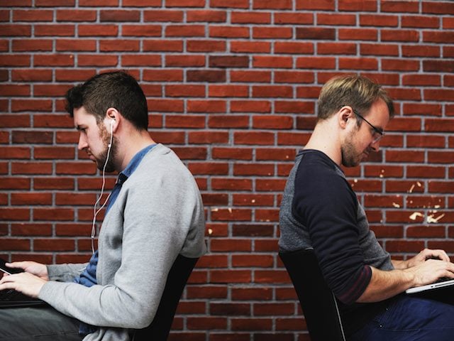 two men working with their backs to each other in a coffee shop