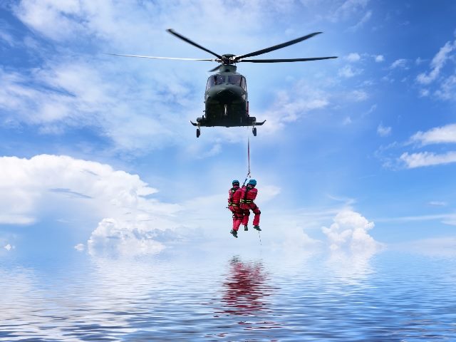  Rescue helicopter in mission sea rescue with two people hanging on to a rope leading up to the helicopter.