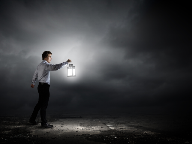 A man holding a lantern searches in the dark