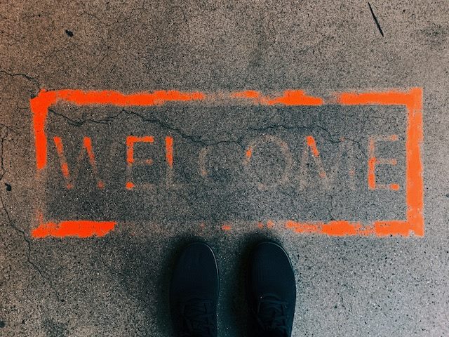 welcome written on  sidewalk with tips of someone's shoes visible