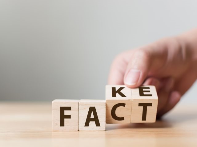 A person's hand holding scrabble tiles that spell fact on one side and fake on the other
