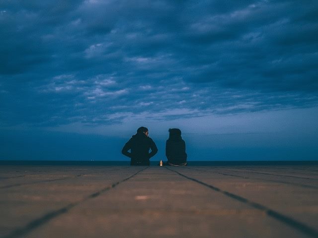 two people sitting on pier at night in middle of conversation